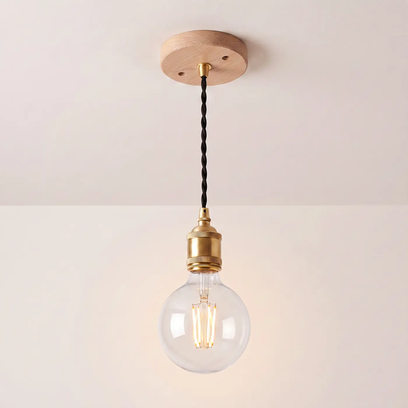 Pendant light with a turned natural oak ceiling rose, black twisted fabric flex and a brass bulb holder, lit with a clear globe filament bulb