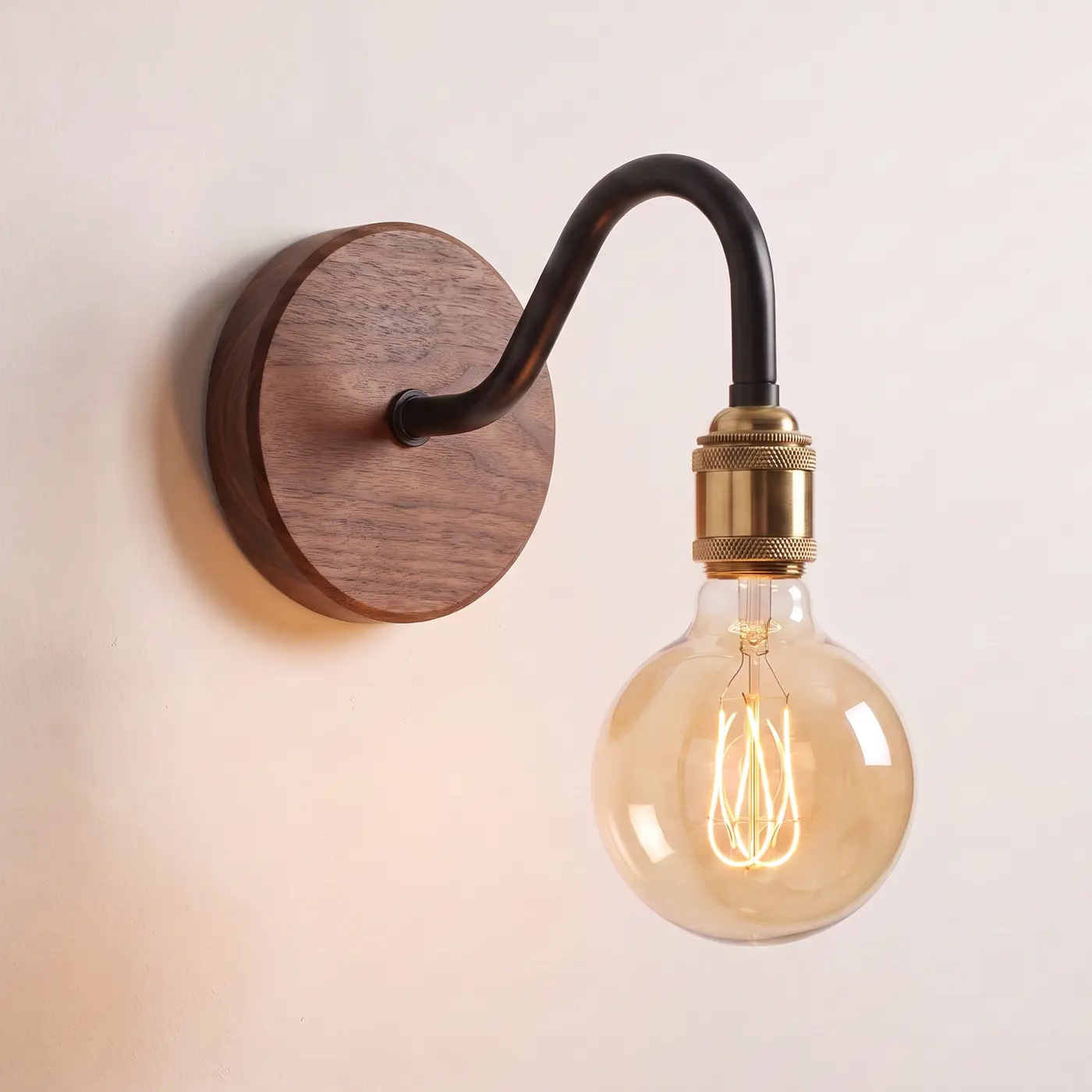 Black swan neck wall light with a brass bulb holder on a solid walnut back plate, mounted on a plain wall with the bulb lit