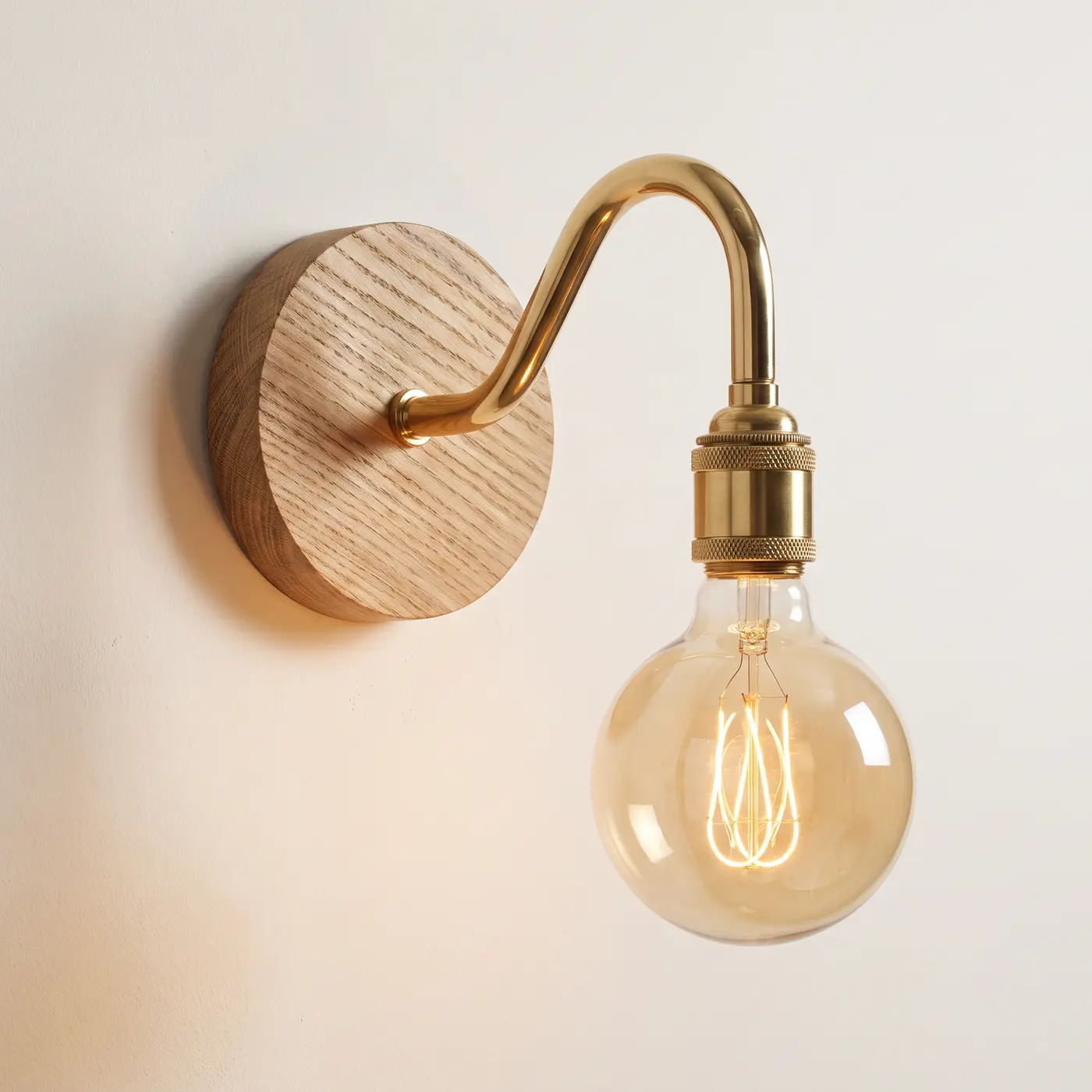 Swan neck wall light with a natural oak back plate, brass swan neck arm and matching bulb holder, lit with a globe filament bulb